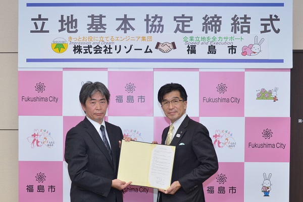 「立地基本協定締結式」のパネルが掲げられており、開いた締結書を手に持つ市長と株式会社リゾームの代表取締役社長の写真