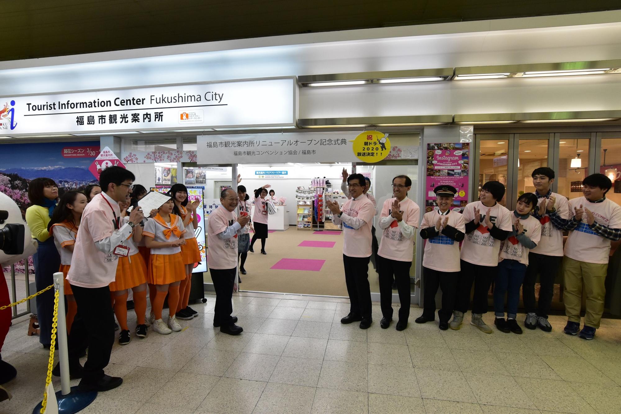 「福島市観光案内所」と書かれた電飾看板が設置された入り口前で、市長や関係者の方々が並び拍手をしている写真