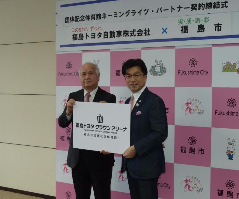 福島市のバックボードの前でスーツを着た市長と男性が「福島トヨタ クラウンアリーナ」と書かれたパネルを持ち、記念撮影をしている写真