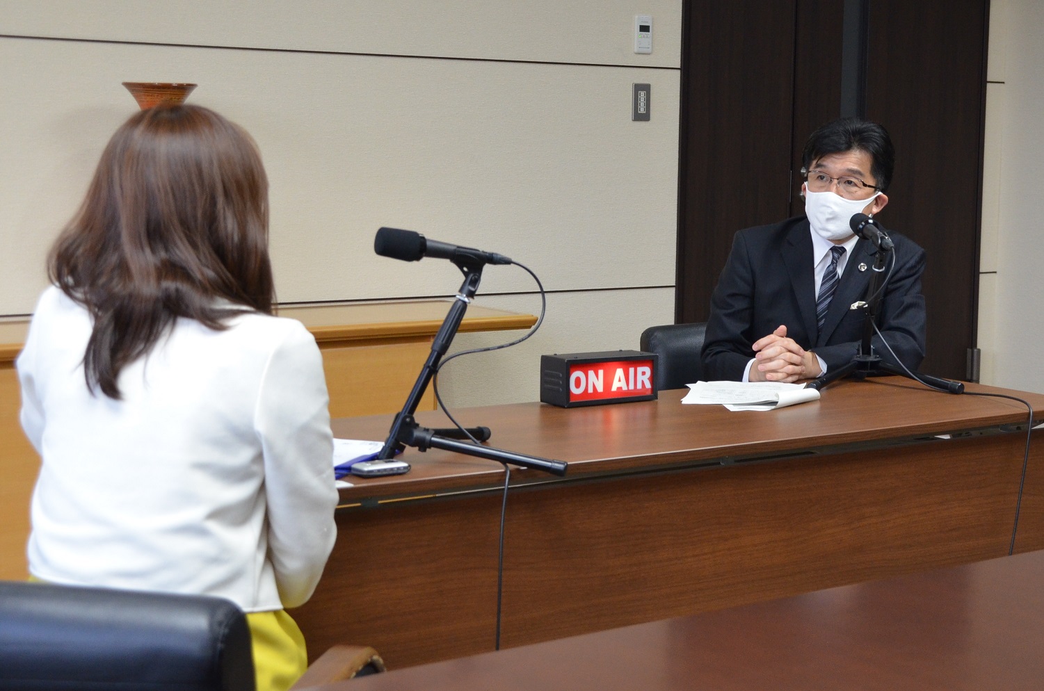 オンエアーランプが机の上に置かれた長机で向かい合って座り、女性と市長がマイクで対談している様子の写真