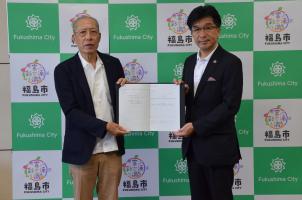 株式会社福良梱包の役員と市長が締結した書類を両手で持ち撮影している写真
