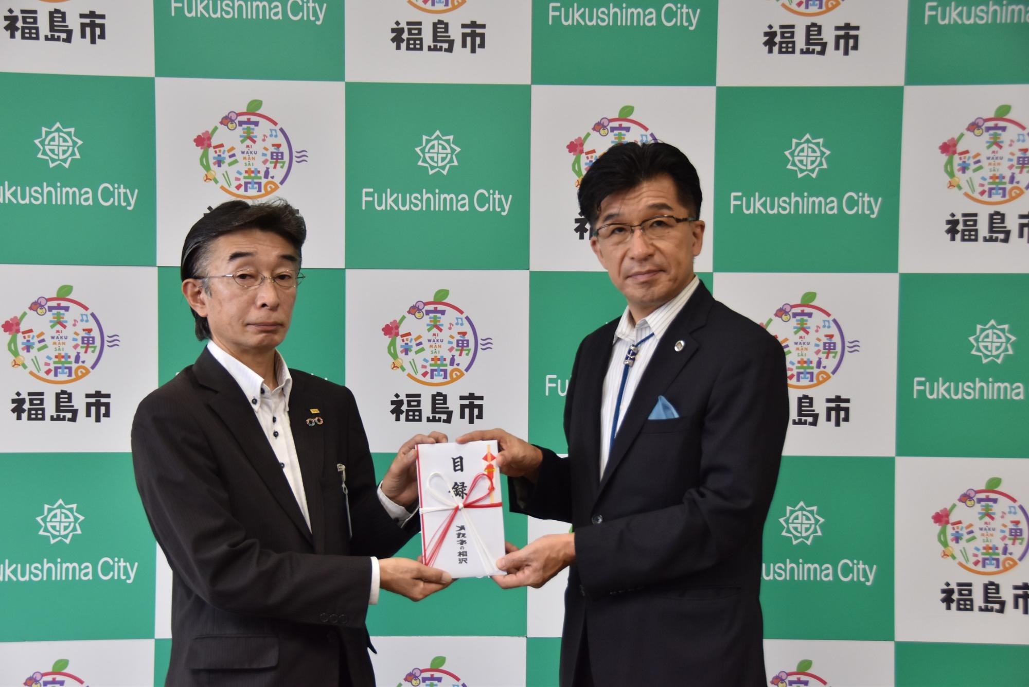 福島市のバックパネル前で、市長と株式会社メガネの相沢様が一緒に目録を手に持っている写真