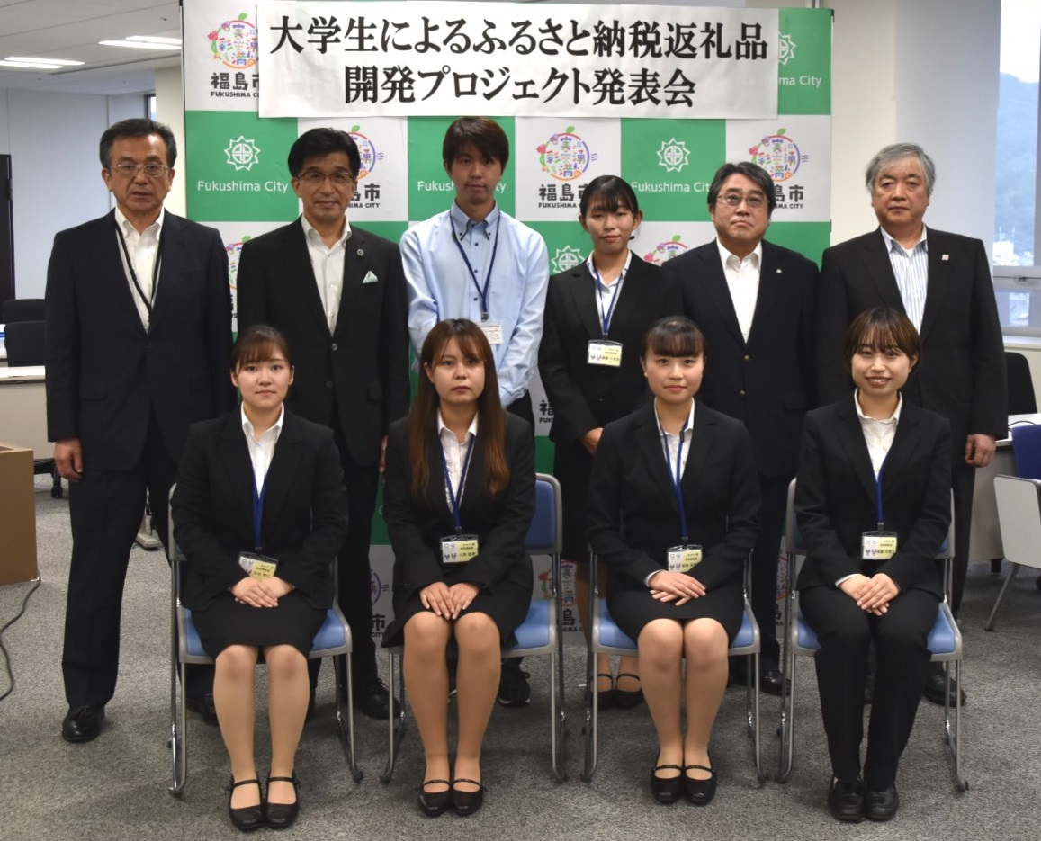 福島市のバックパネルに「大学生によるふるさと納税返礼品開発プロジェクト発表会」と書かれた横断幕がある前で、市長とスーツ姿の大学生と関係者10名が2列に並んでいる写真