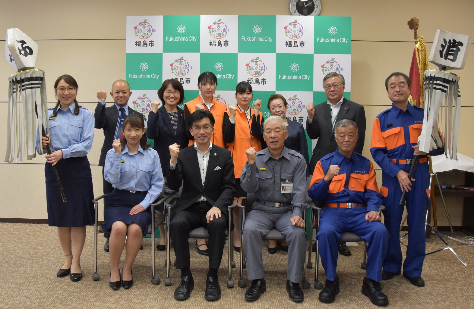 福島市のバックパネル前で、市長と関係者が並んでおり纏を手に持っている写真