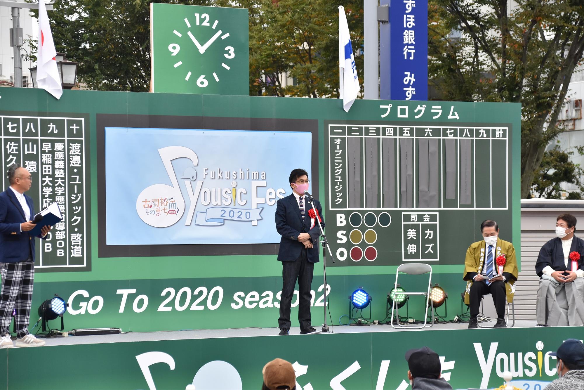 野球場を見立てた野外特設ステージの上で話をする市長と関係者の写真