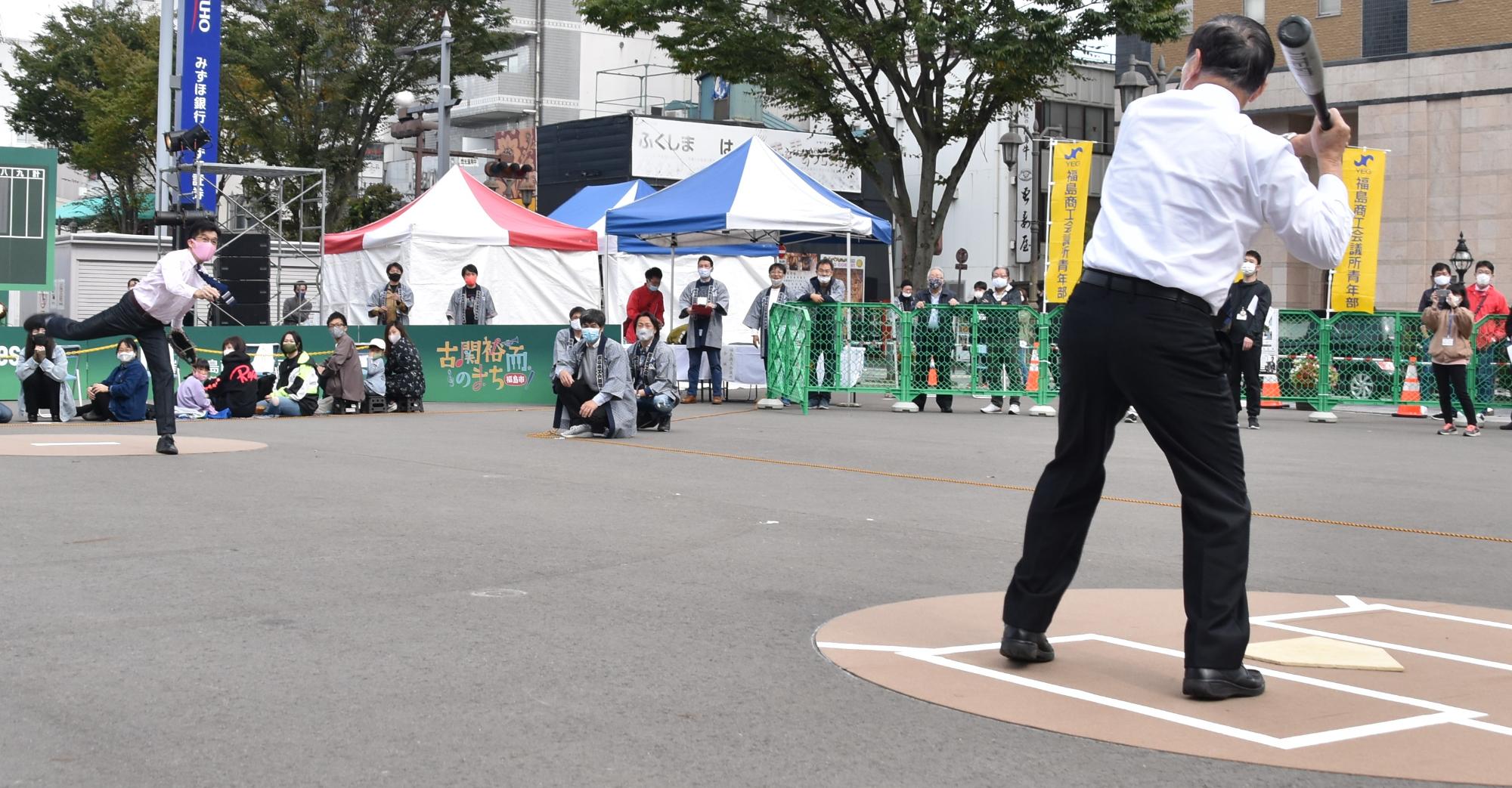 市長がホームベースに立つバッターに向かってボールを投げている写真