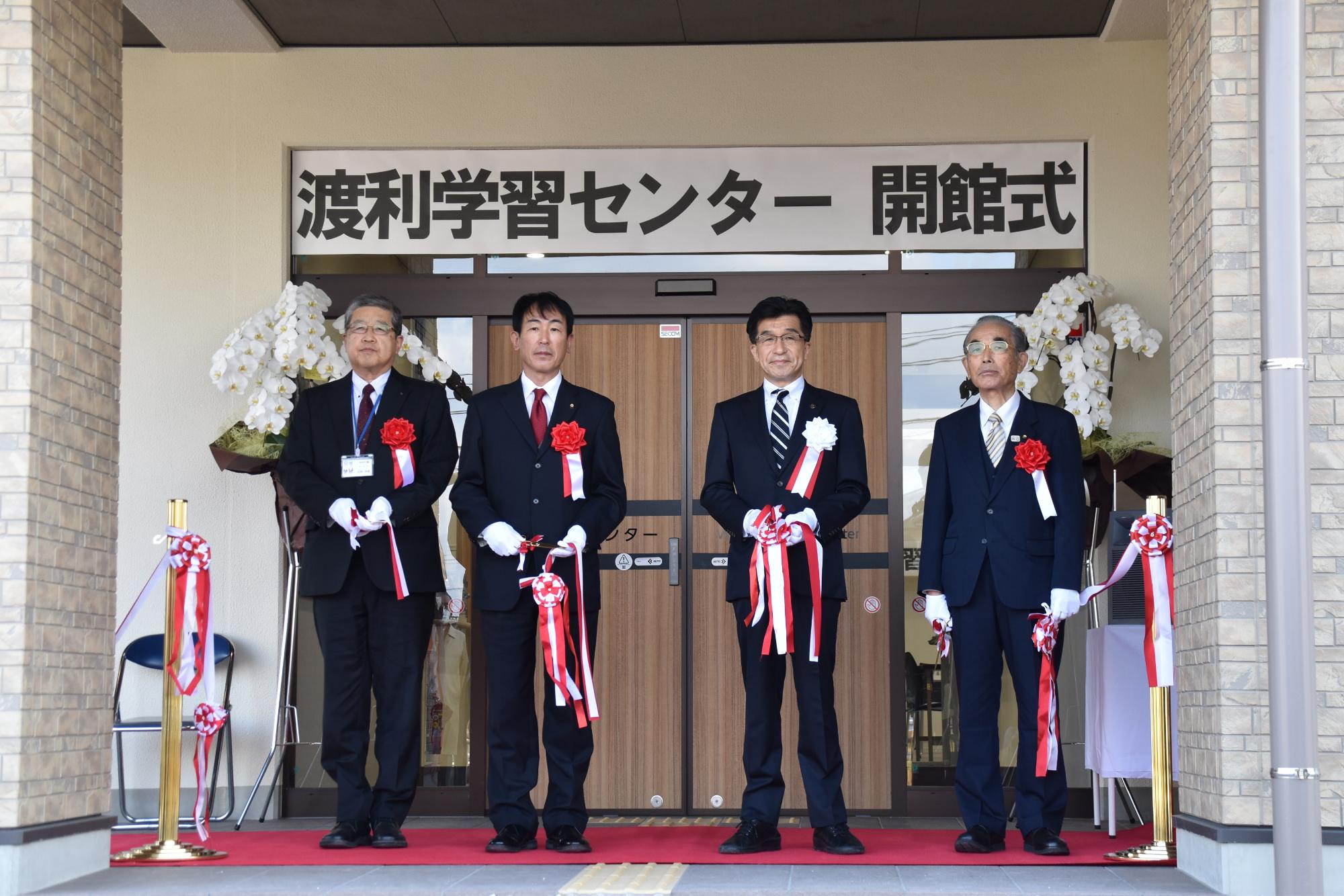 「渡利学習センター開館式」の横断幕が入り口の上に飾られ、市長と関係者が入り口前のレッドカーペットの上でテープカットを行っている写真