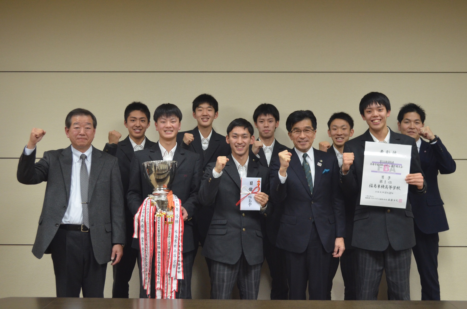 市長と制服をきた男子生徒8名と男性が2列に並び、前列の生徒は優勝カップや金封や賞状を手に持ち、全員でガッツポーズして記念撮影している写真