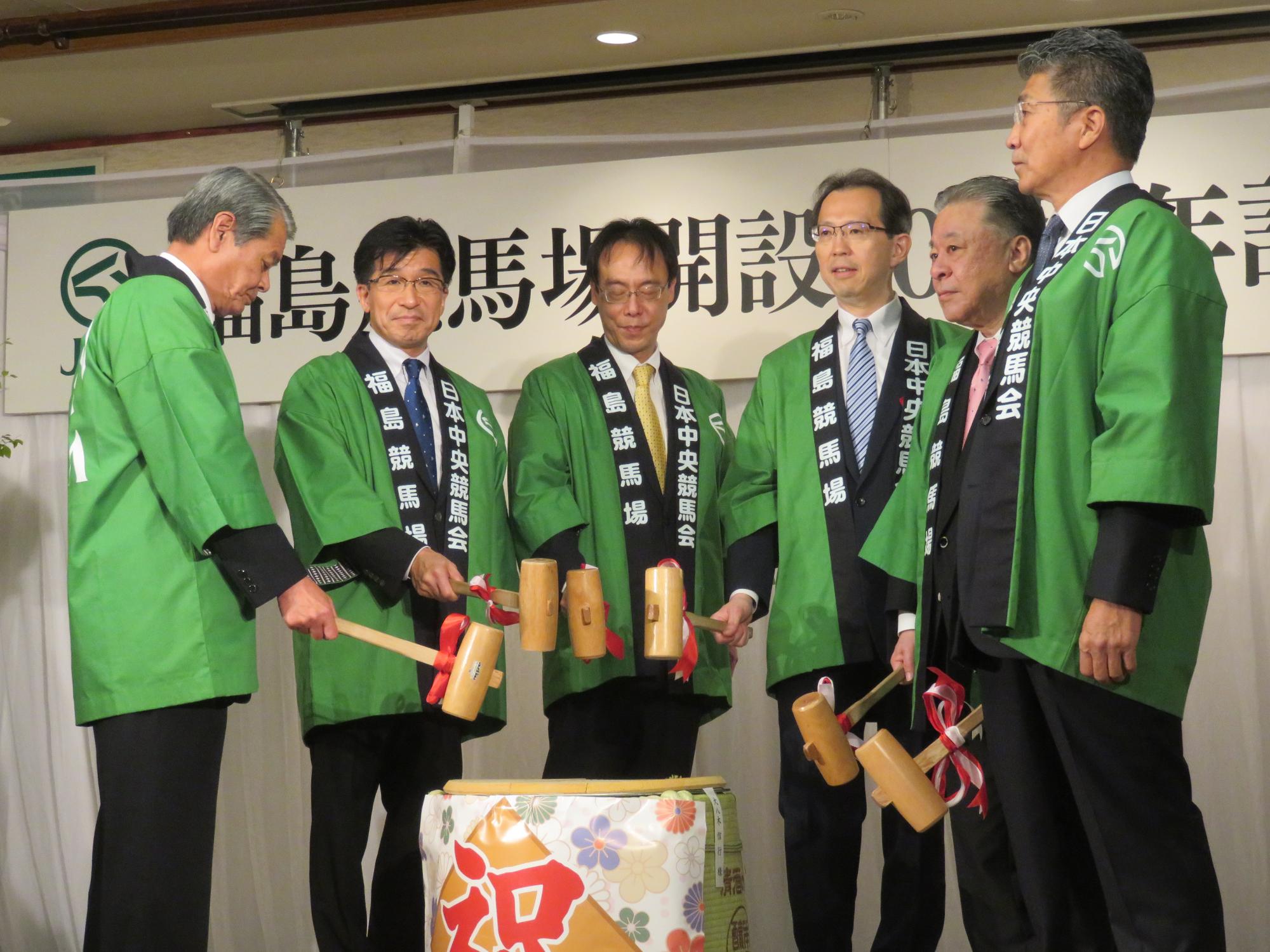 緑色のはっぴを着た市長と関係者が小槌を手に持ち、鏡開きをしている写真