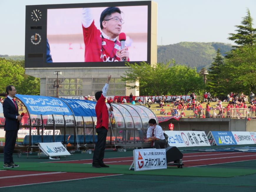 市長がグランドで右手をあげて話をしているところが、大型ビジョンに映し出されている写真