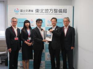 東北地方整備局のバックパネルの前で、市長他男性3名、女性1名が立ち市長が男性と要望書を持っている写真