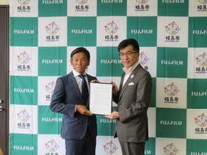 バックパネルの前で、男性と市長で協定書を持っている写真