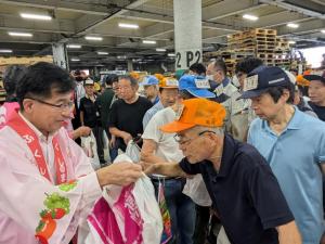 法被を着た市長が並んでいる男性にビニール袋を手渡している写真