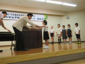 市長がステージ上で女子児童に賞状を手渡している写真