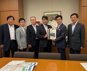 執務室で市長を含めて6名が立ち、市長と男性が要望書を持っている写真