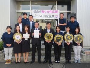 建物入口で「福島市働く女性応援ゴールド認証企業」の幕を持っている人の前で賞状や「ゴールド」の文字を装飾したうちわを持った人が横に整列している写真