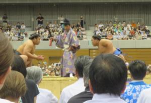 土俵上で黒の締込をした若元春と青の締込をした若隆景が、行司の前で腰を下ろして向かい合っているところを客席から撮影した写真
