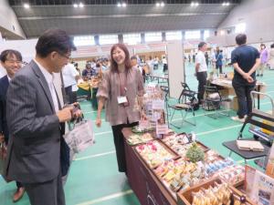 女性が担当しているスペースに陳列してある多くの商品を市長が見ている写真