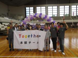 体育館で「Together本部チーム」と書かれた横断幕を持った参加者の集合写真