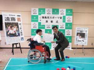 「福島市スポーツ賞表彰式」と書かれた幕が貼られたバックパネルの前で、車いすの女性と市長で賞状を持っている写真