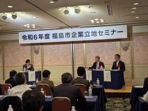 「令和6年福島市企業立地センター」と書かれた横断幕がある会場で、ステージに3名の男性がパネラーとして座り、多くの参加者が座って聞いている写真