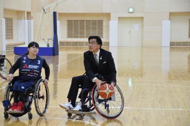 車いすに乗り、バスケットボールでドリブルする市長とU-25女子車いすバスケ日本代表の選手の写真