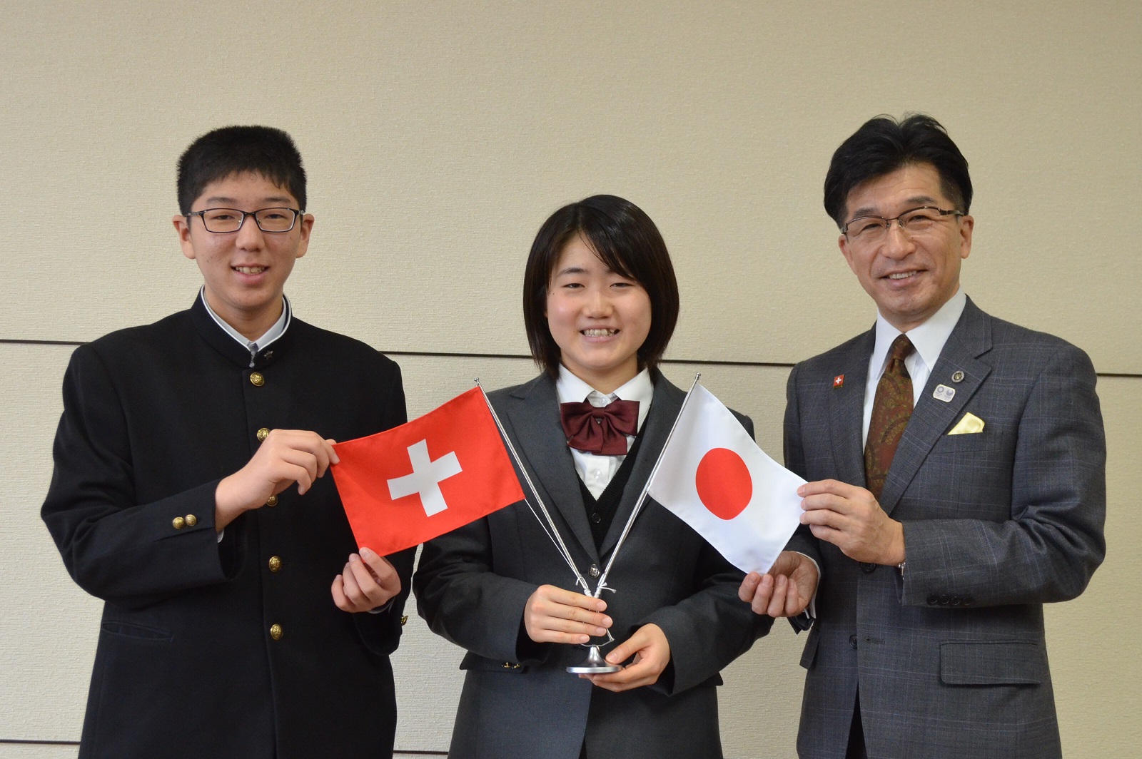 真ん中の女子生徒が日本とスイスの手旗を持ち、日本の手旗を市長、スイスの手旗を男子生徒が持ち広げ、記念撮影している写真