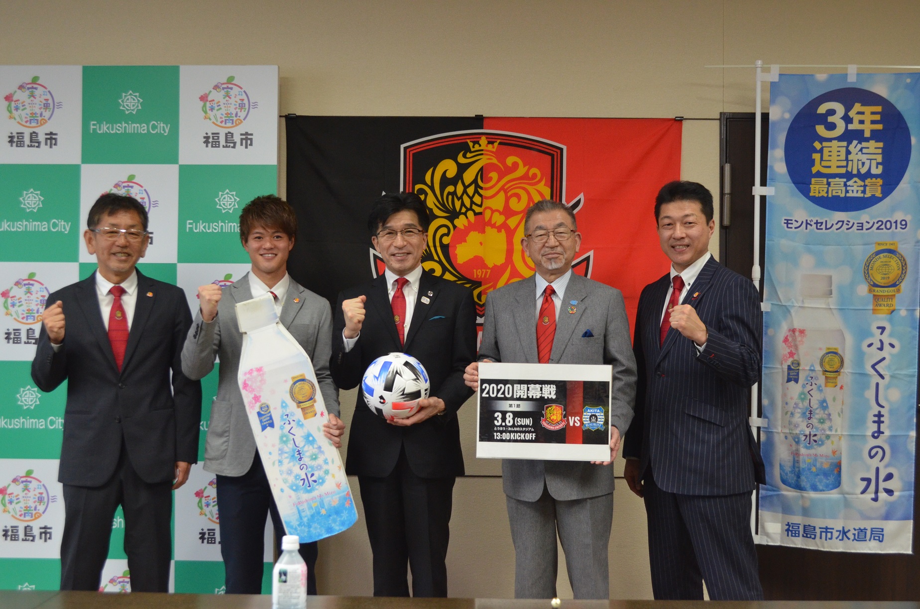 福島市のバックボードと福島ユナイテッドFCの応援旗とふくしまの水ののぼり旗の前でサッカーボールを手に持った市長と男性4名がガッツポーズをして記念撮影をしている写真