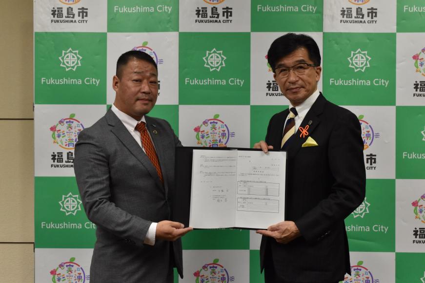 バックパネルの前で、市長と男性で協定書を持っている写真