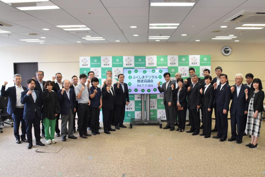 「ふくしまデジタル推進評議会」の文字が映し出されたモニターを中心に20名ほどの参加者が分かれて、ハの字型に並びガッツポーズをしている写真
