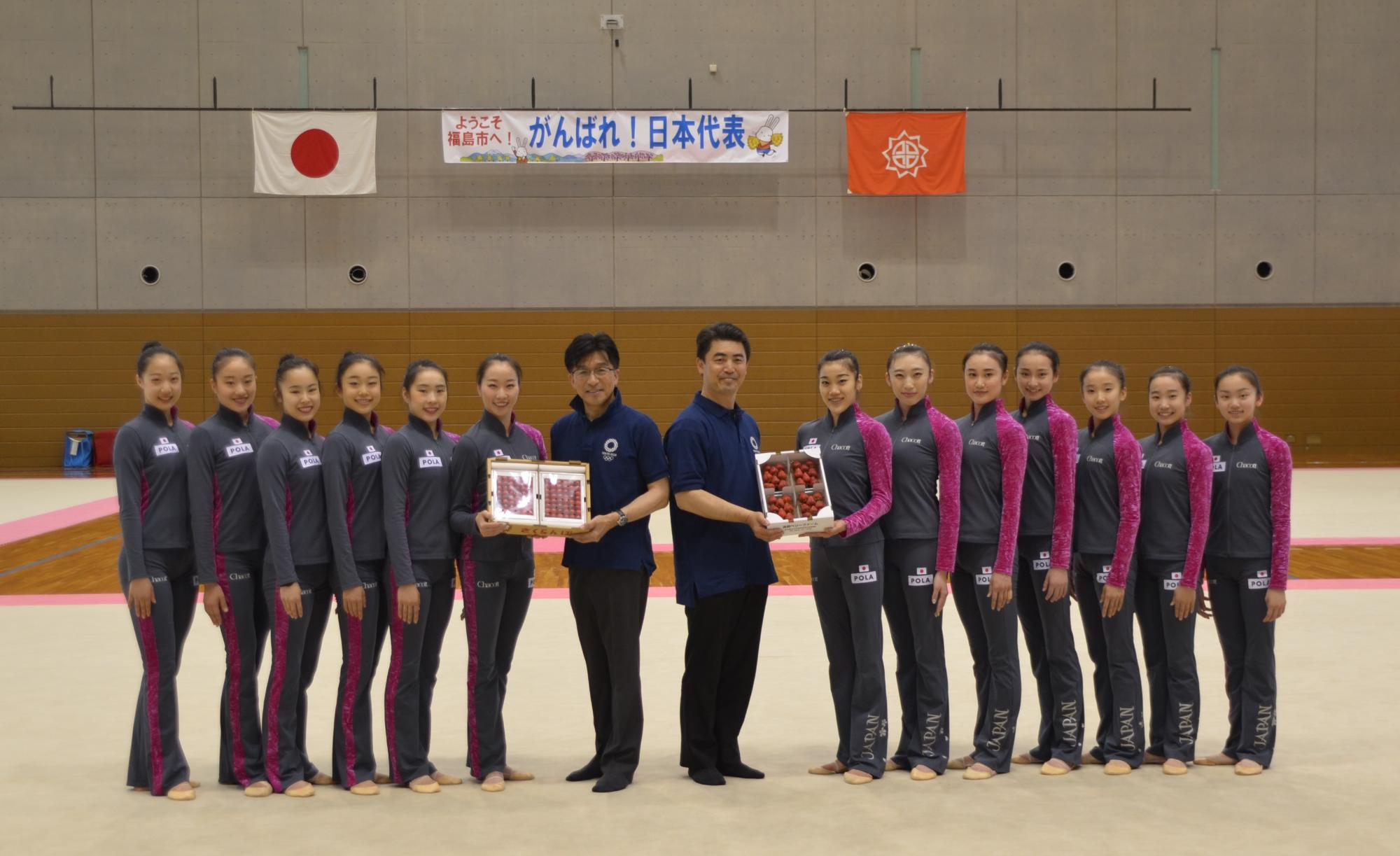 「がんばれ!日本代表」と書かれた横断幕と日本国旗と福島市章が掲げられた体育館の中で、市長と男性と新体操日本代表選手が並び記念撮影している写真