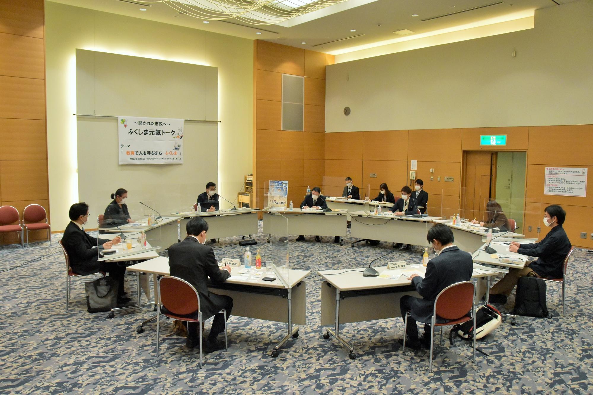 円形に並べられた机に、市長と関係者が椅子に座り意見交換を行っている写真