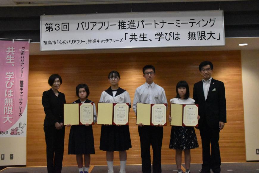市長と女性の間に表彰された男子生徒1名、女子生徒3名が立ち、それぞれ賞状ファイルを広げて持っている写真