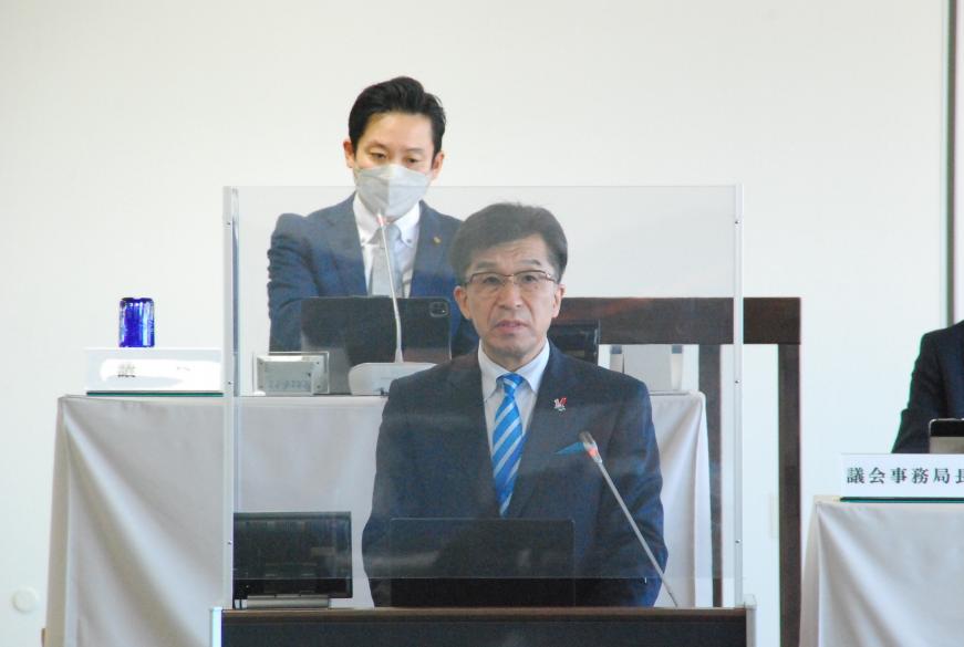 議長と事務局長が自席に座り見ている前で、檀上に立つ市長が話をしている写真