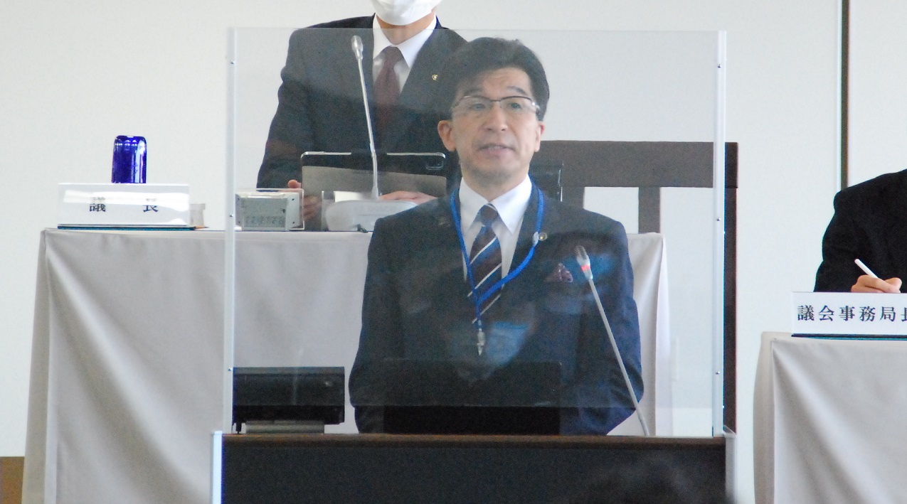 市長がアクリル板を追加した演台に立って話をしている写真
