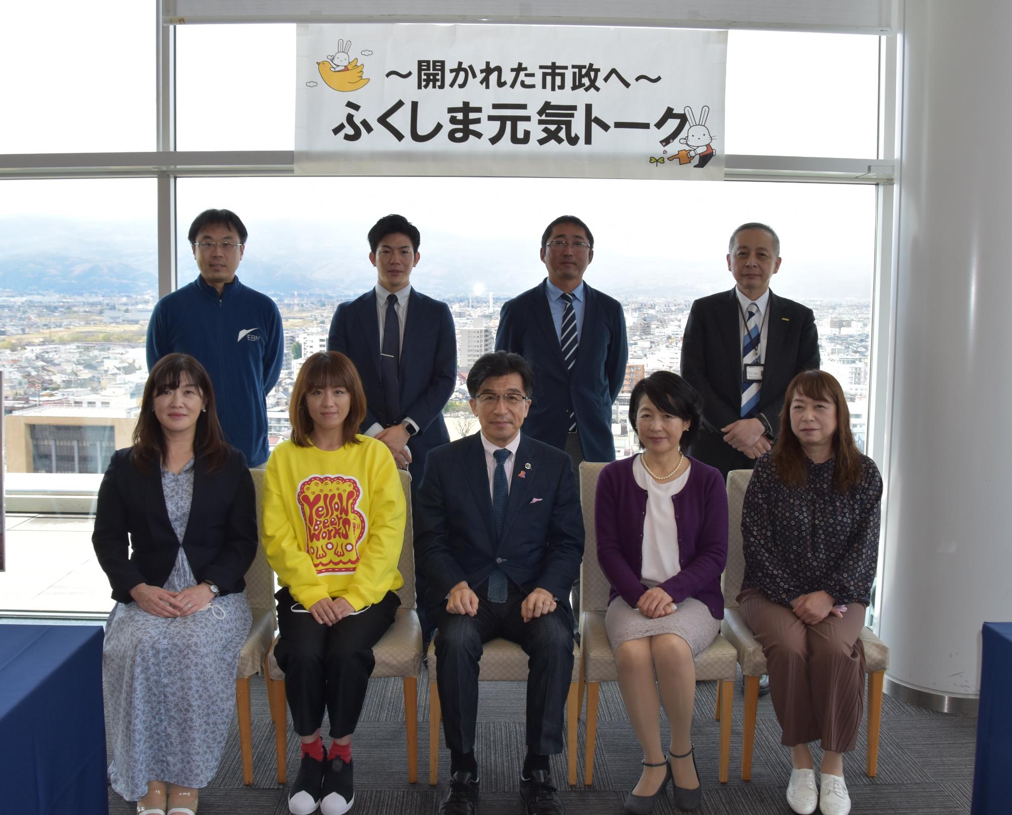 大きな窓の上部に設置された「~開かれた市政へ~ふくしま元気トーク」の横断幕の前で市長と関係者が2列に並んだ記念写真