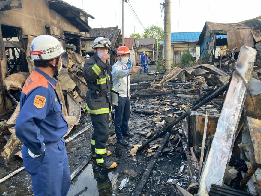 ヘルメットを着用した市長と消防服を着た男性2名が火事で焼けた家を見ながら話しをしている様子の写真