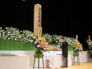 白い花が飾られており、慰霊碑が祭壇の中央にある前で哀悼の意を捧げる市長の写真