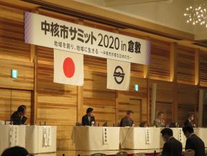 「中核市サミット2020in倉敷」の吊りパネルがあり、壇上の席に座っている市長と関係者の写真