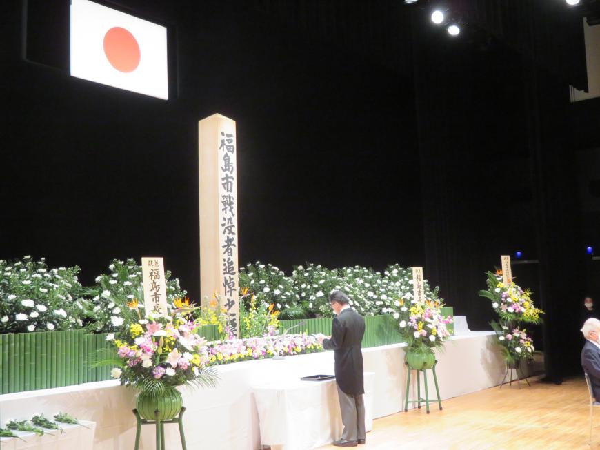 花が飾られた戦没者追悼の祭壇の前で、市長が哀悼の意を述べている写真