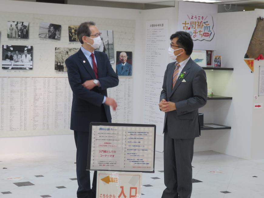 壁に古関裕而さんの資料が貼られた部屋で市長と男性が話をしている写真
