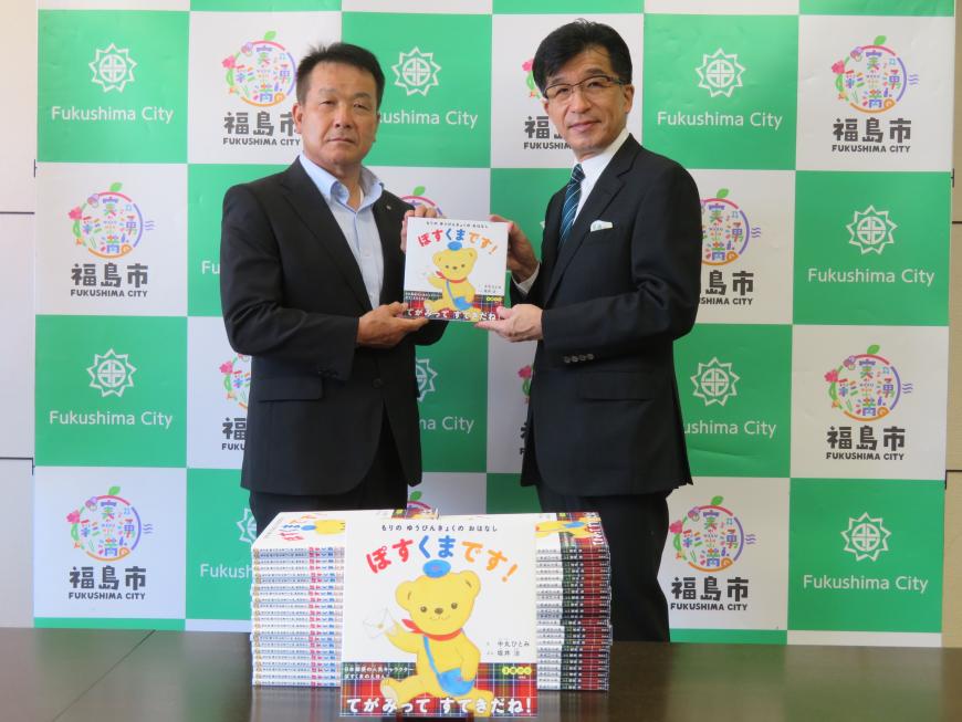 市長と男性で絵本を持って立ち、その前には寄付された絵本が置いてある写真