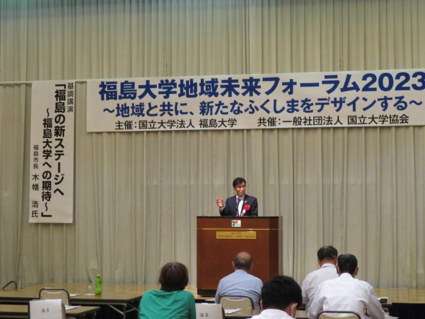 「福島大学地域未来フォーラム2023」と書かれた横断幕があるステージで、市長が演台で参加者に向けて話をしている写真