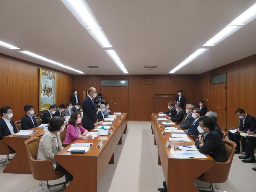 対面式に座っている参加者の1人が自席で立って話をしている写真