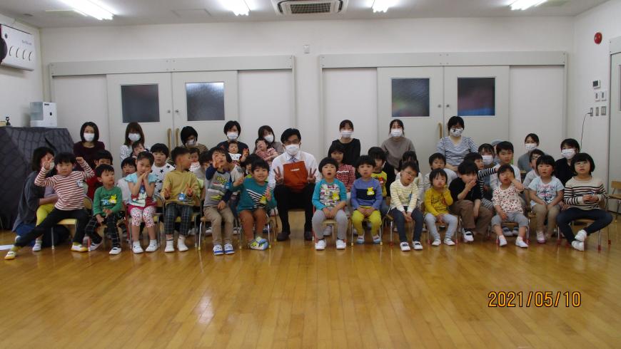 中央で椅子に座り両手でピースサインをしている市長と、その左右に座った園児達や関係者たち複数名が記念撮影している写真