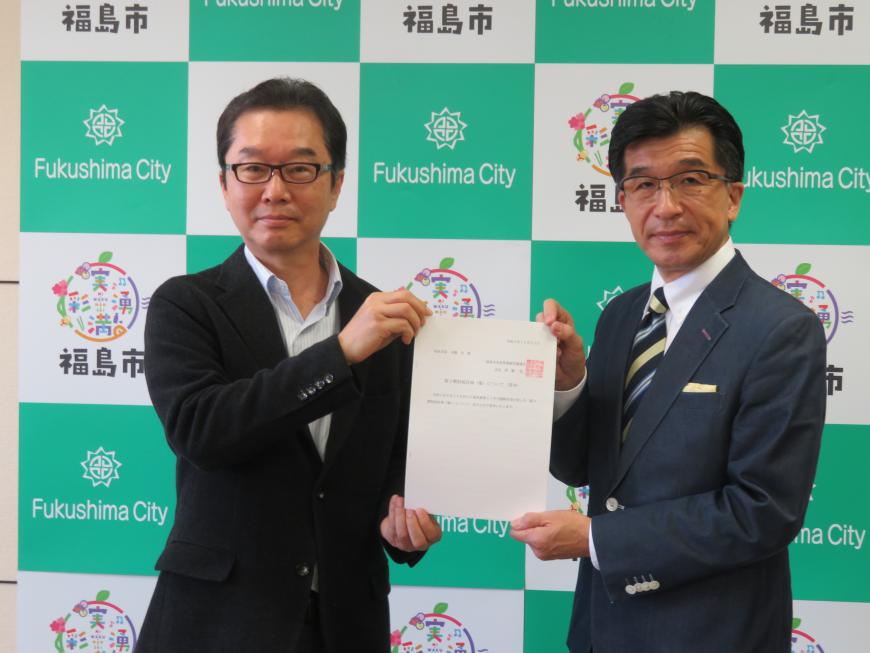 バックパネルの前で、市長と男性で答申書を持っている写真