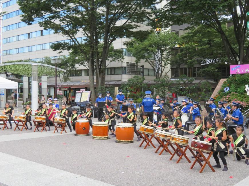 屋外の広場で子どもたちのマーチングバンドと太鼓の演奏が行われている写真