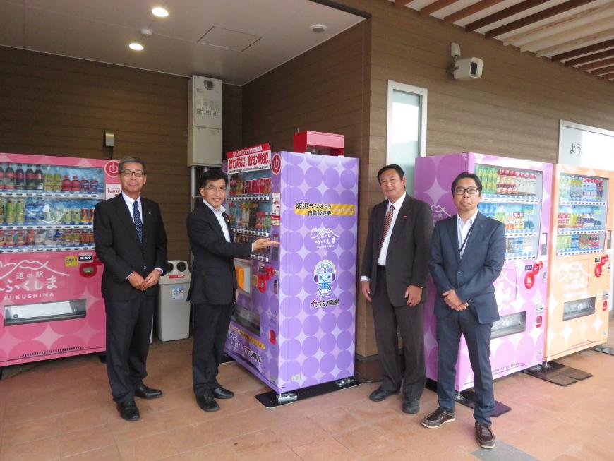 自動販売機の横に市長を含む男性4名が2名ずつ並んでいる写真