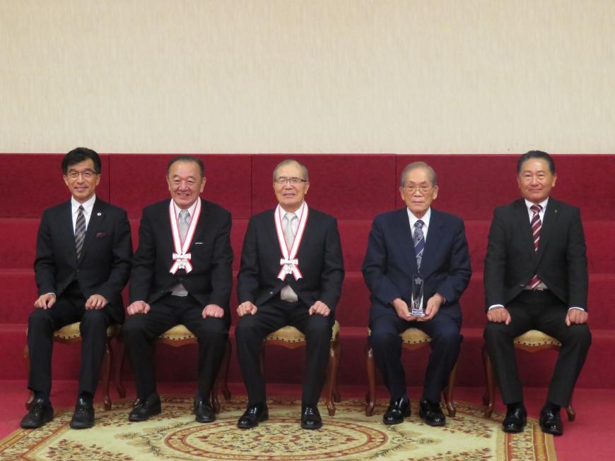 市長と職員の男性との間にメダルをかけた男性2名、盾を持った男性1名が座っている写真