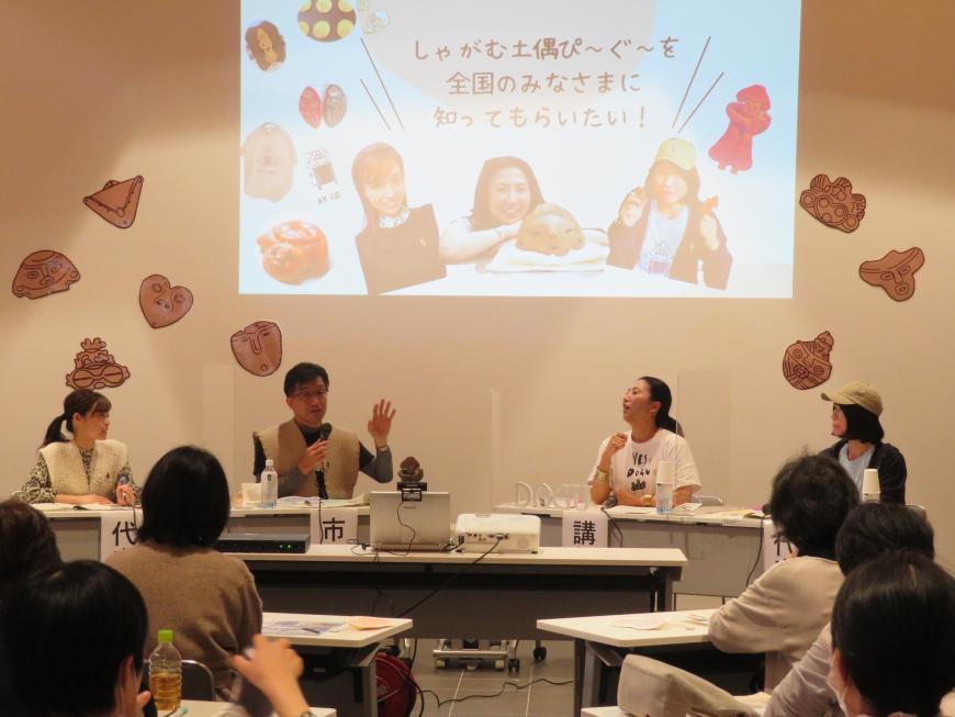 円形に並べられた机に座っている参加者に向けて、市長がマイクを持って話をしている写真